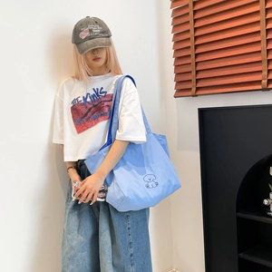 Détail du sac cabas en toile bleu clair avec broderie de chien porté par le mannequin