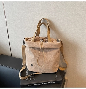 Detail of khaki drawstring bucket bag showing water-resistant nylon texture and metal emblem