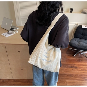 Vista laterale della borsa tote crema con trama stropicciata e scritte blu moda