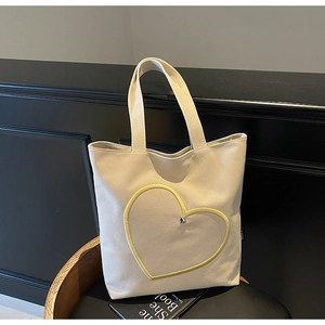 Vue détaillée du sac cabas en toile crème avec broderie cœur dorée sur meuble en bois