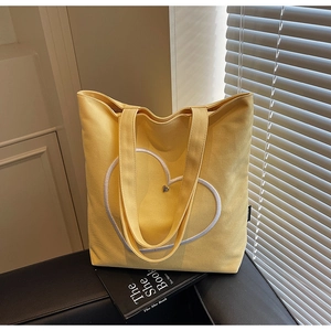 Détail d'un cabas en toile jaune avec cœur brodé posé sur un siège en cuir chic