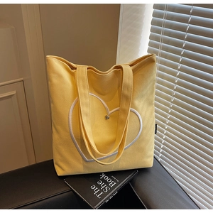 Détail du cabas en toile jaune avec broderie cœur blanche et breloque métallique