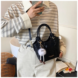 Détail du sac seau noir motif crocodile avec un pendentif en peluche blanche mignon