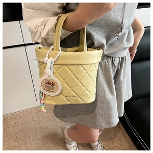 Detail of yellow quilted tote bag featuring a cute capybara charm and brand logo