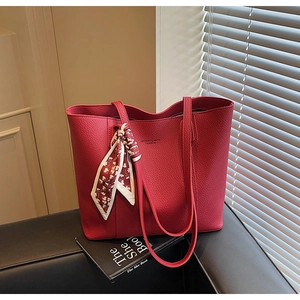 Detail of red lychee leather tote bag with printed silk scarf handle on black sofa