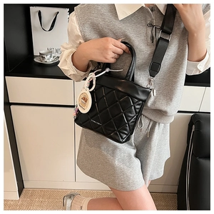 Detail of black quilted bucket bag with wide strap and cartoon biscuit pendant