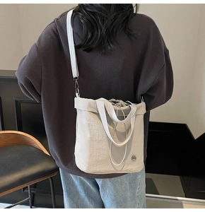 Back view of grey canvas drawstring bucket bag worn as a crossbody with woven handle