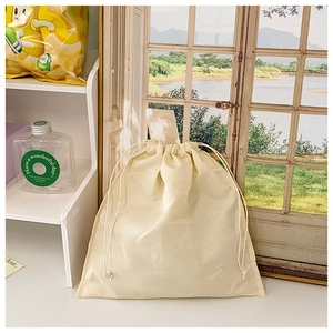 Detail of a natural cotton drawstring storage bag with woven texture on a white table