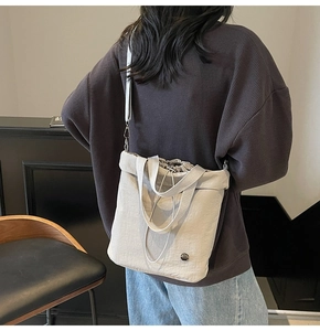 Detail of light gray water-resistant nylon bucket bag with drawstring closure and metal logo
