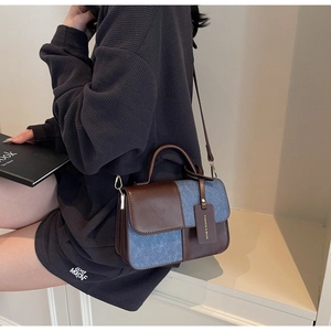 Detail of blue denim and brown leather stitching on a mini crossbody square bag