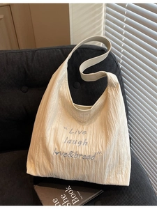 Minimalist pleated cream tote bag with blue embroidery on a modern grey chair