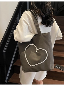 Sac fourre-tout en toile grise à motif cœur porté par un mannequin sur des escaliers en bois