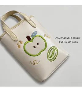 Detail of cream white apple-shaped crossbody bag with Nice embroidery on denim background