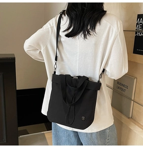 Detail of black canvas bucket bag with adjustable shoulder strap and metal logo on side