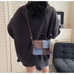 Detail of color-block crossbody bag featuring brown leather and blue denim patchwork