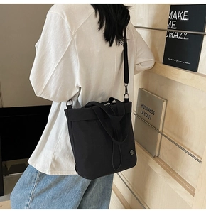 Detail of black nylon bucket bag with metallic logo and adjustable crossbody strap