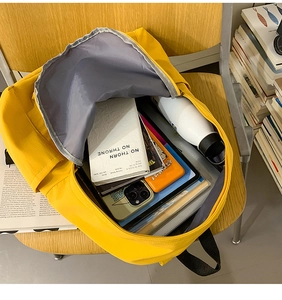 Detailed view of open bright yellow backpack on a wooden chair with school supplies