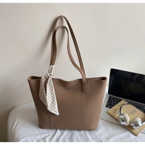 Detailed shot of tan faux leather tote with logo branding and decorative silk scarf detail