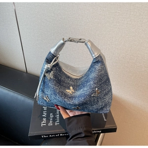 Detail der blauen Jeans-Umhängetasche mit Metallschmetterlingen und Silbergriff