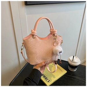 Détail du sac à main rose motif serpent avec poignée nouée et breloque pompon blanc