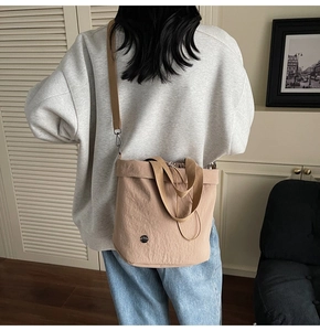 Close-up of beige nylon bucket bag with brown woven handles and adjustable shoulder strap