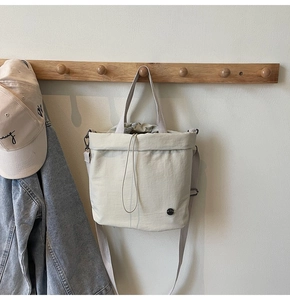 Detail of off-white drawstring tote with adjustable strap and small black logo