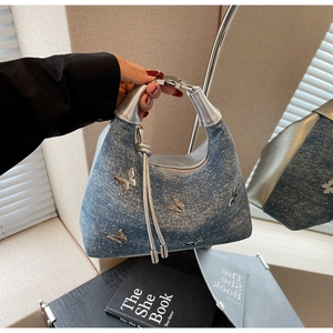 Détail du sac demi-lune en denim avec papillons argentés et pendentifs à franges chic