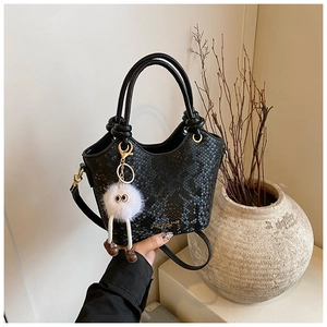 Détail du sac seau noir motif serpent avec pendentif peluche blanc et texte mode