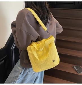 Detail of yellow nylon drawstring bucket bag showing texture and wide woven shoulder strap