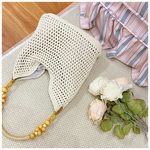 Detail of hollow crochet weave and yellow wooden bead handle on a cream straw tote bag