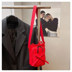 Close-up of red crossbody bag with bow detail and adjustable nylon strap in a shop setting
