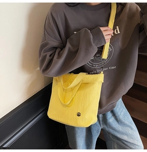 Model wearing a bright yellow canvas bucket bag with adjustable strap in a home setting