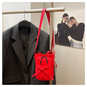 Detail of red nylon crossbody bag with bow decoration and black zippers on metal hanger