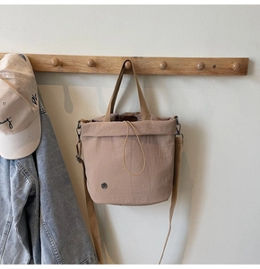 Light brown drawstring bucket bag displayed on a wooden hook with soft casual background