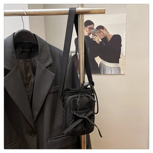 Detail of black nylon crossbody bag with bow drawstring closure on a studio hanger