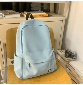 Detail of light blue minimalist backpack with MYJC tag on a wooden chair background