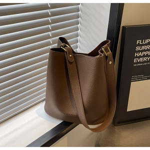 Close-up of brown lychee grain leather bucket bag with wide strap and gold hardware detail