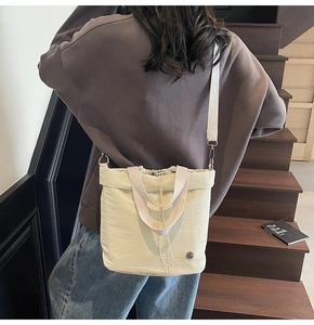 Beige canvas drawstring bucket bag worn crossbody against casual lifestyle background