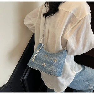 Detail der blauen Denim-Schultertasche mit silbernen Schmetterlingsanhängern und Mondform