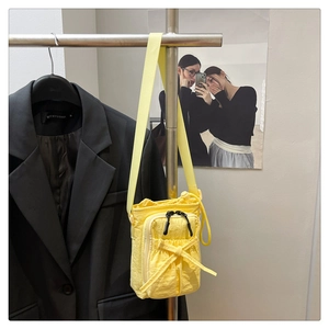 Detail of yellow nylon crossbody phone bag with bow accent and multi-pocket design