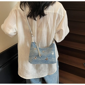 Sac sous le bras en jean bleu avec papillons argentés porté à l'épaule par un mannequin