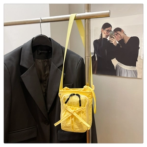 Detail of a bright yellow mini crossbody bag with nylon texture and ribbon decor