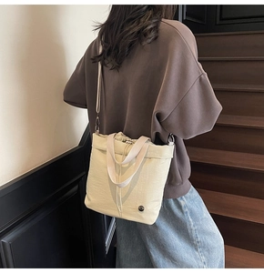 Detail view of cream drawstring bucket bag with dual handles and metal logo detail