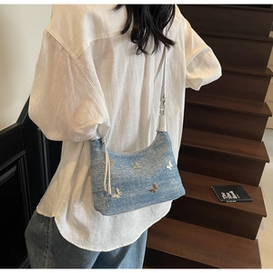 Détail du sac demi-lune en denim bleu clair avec breloques papillon sur escalier bois