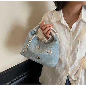 Detailed close-up of light blue denim handbag with silver bow charms and metal handle