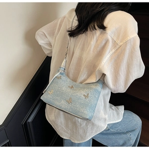 Detail der hellblauen Denim-Achseltasche mit silbernen Schmetterlingen am Modell