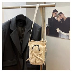 Detail of cream nylon crossbody bag featuring front zipper pocket and decorative bow