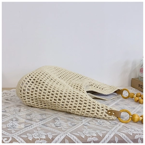 Detail of straw woven beach bag featuring large wooden bead handle and cotton mesh texture
