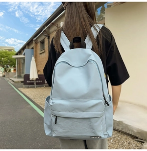 Outdoor shot of light blue minimalist nylon backpack with side pockets and front zipper