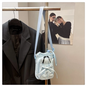 Close-up of light blue pleated crossbody bag with bow detail on a hanger